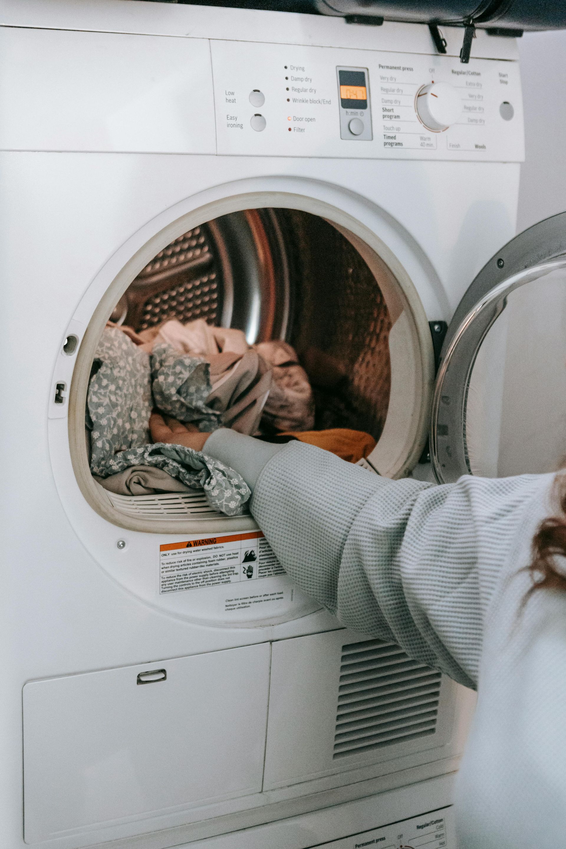 A woman is putting clothes in a dryer.