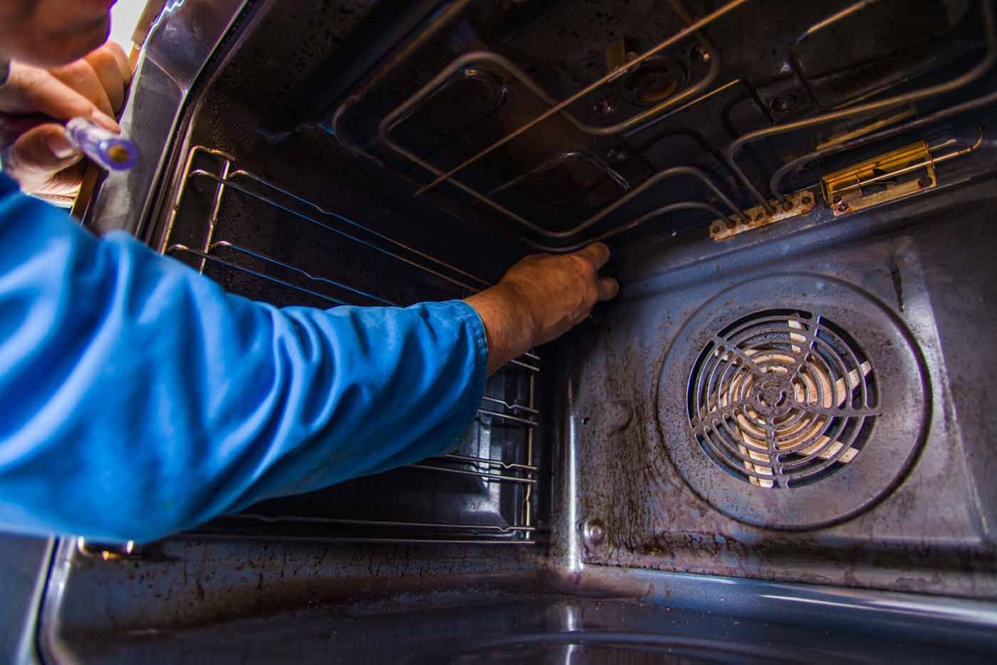 A man in a blue shirt is cleaning a dirty oven.