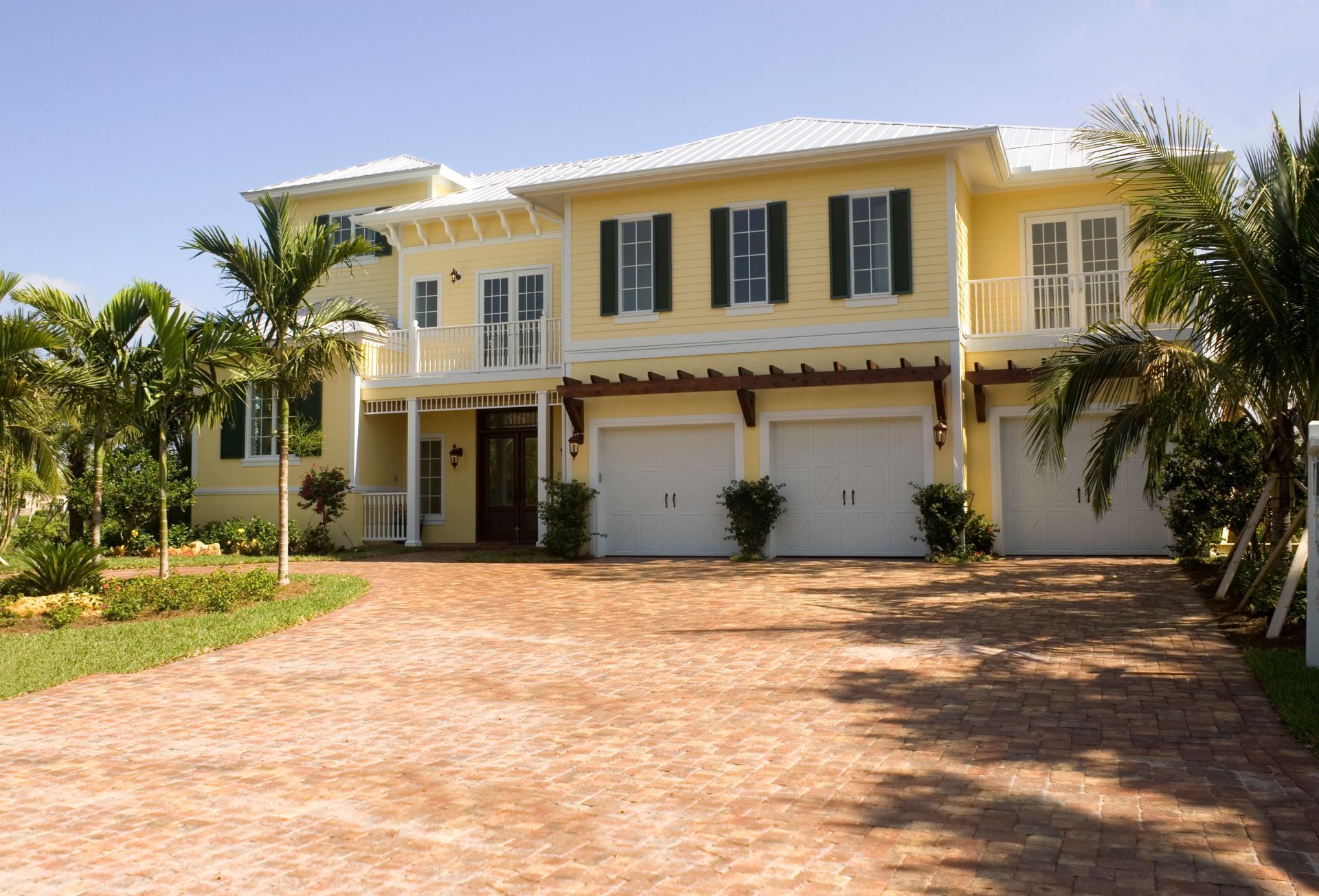 A large yellow house with a brick driveway in front of it