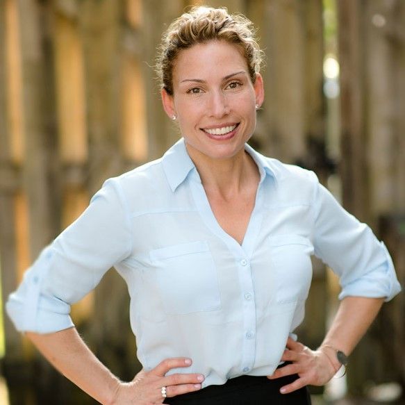 A woman in a light blue shirt is smiling with her hands on her hips