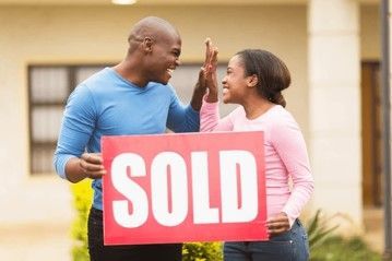A man and a woman are giving each other a high five while holding a sold sign.
