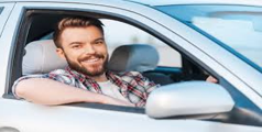A man with a beard is sitting in a car and smiling.