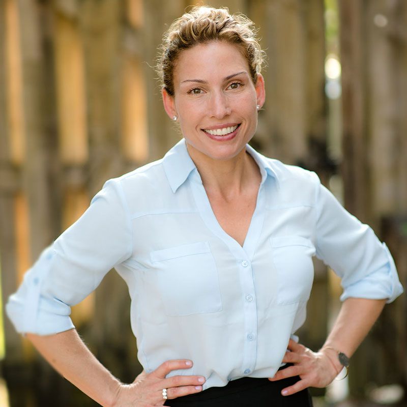 A woman in a light blue shirt is smiling with her hands on her hips