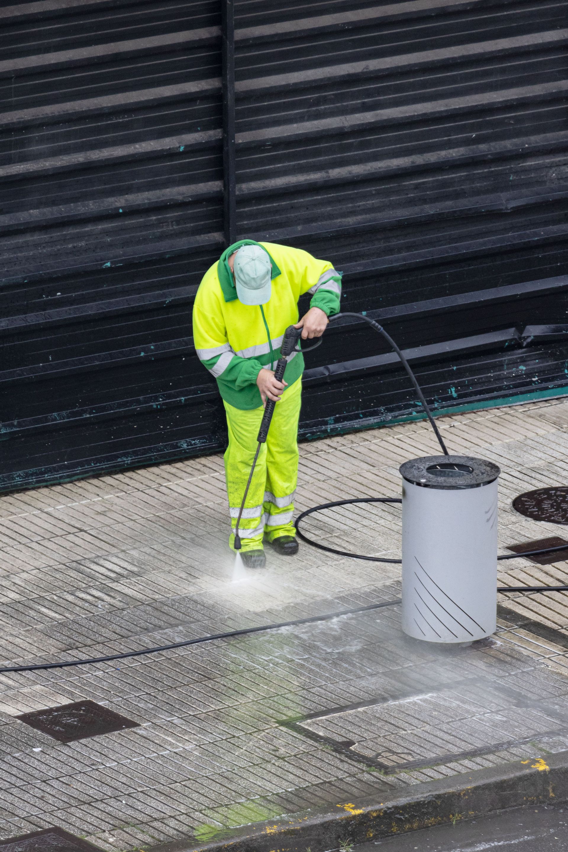 A worker cleaning a sidewalk with high pressure water