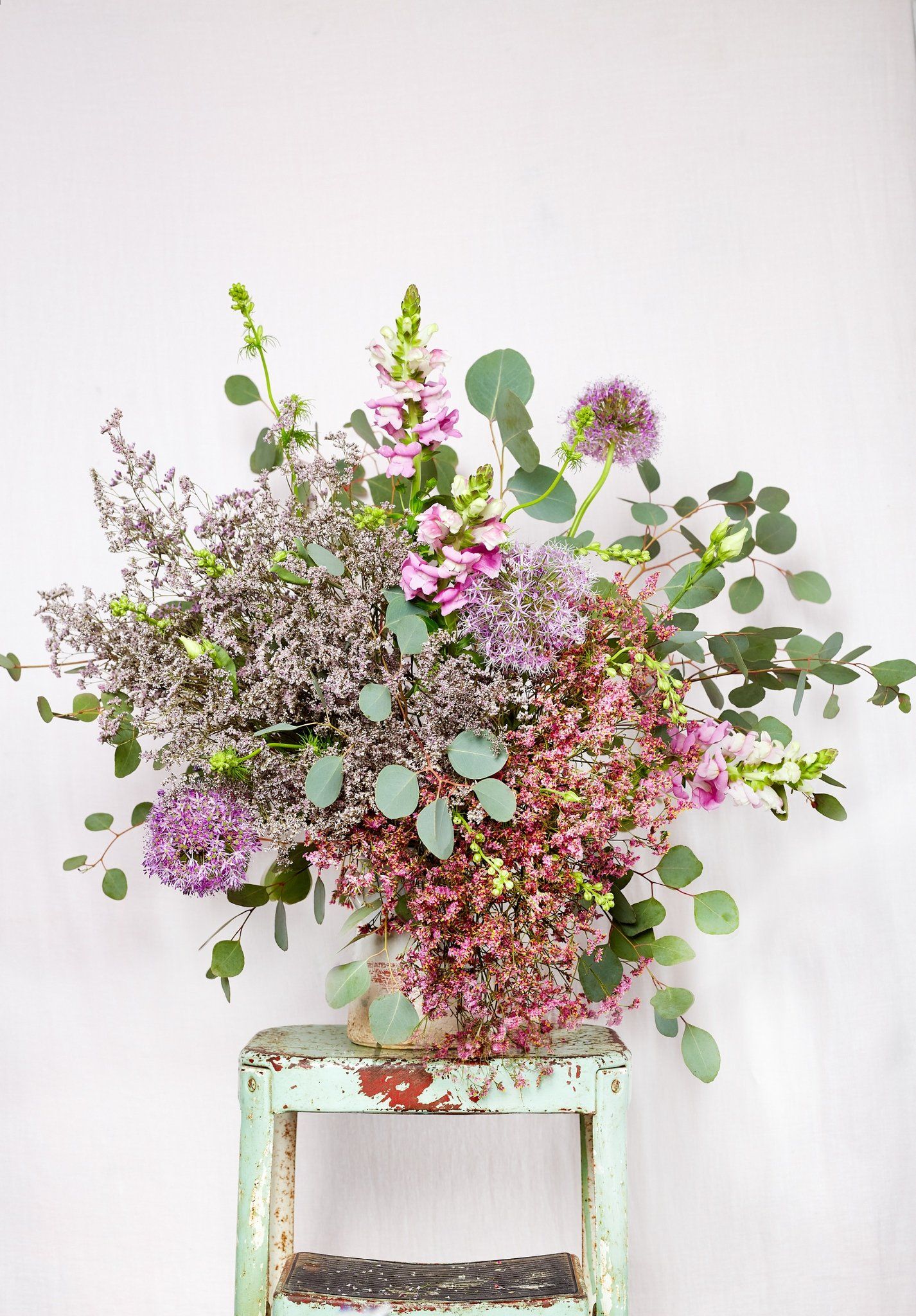 A bouquet of flowers is sitting on a green stool against a white wall.