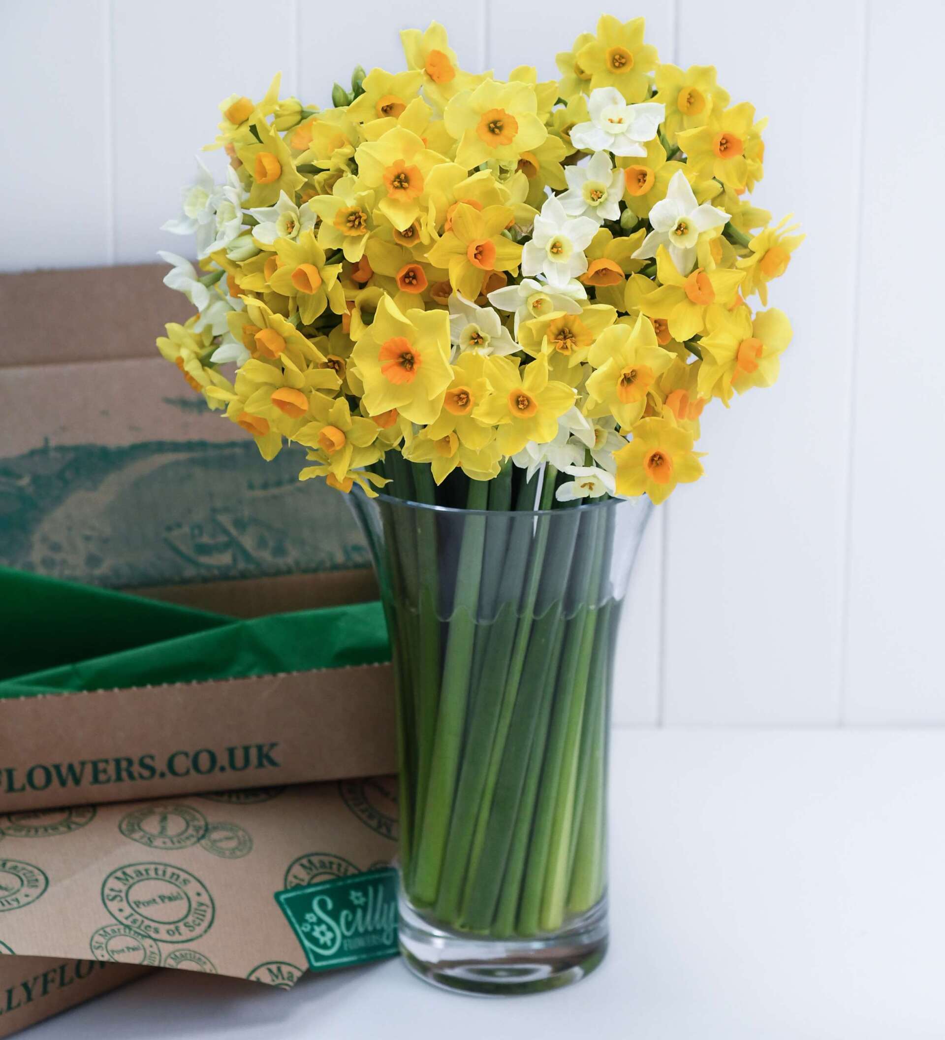 A vase filled with yellow and white flowers next to a box that says flowers.co.uk
