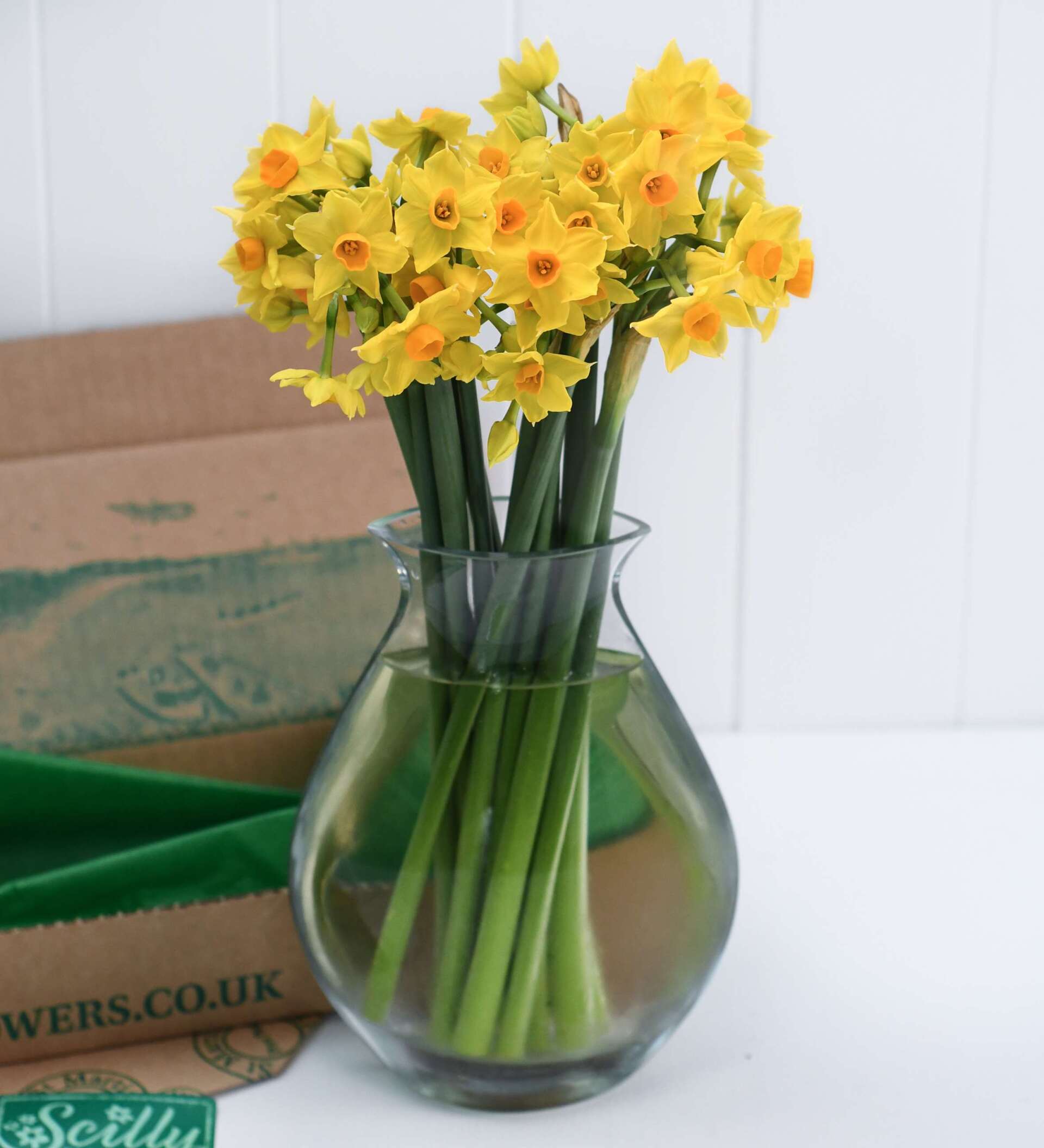 A vase filled with yellow flowers next to a box that says flowers.co.uk