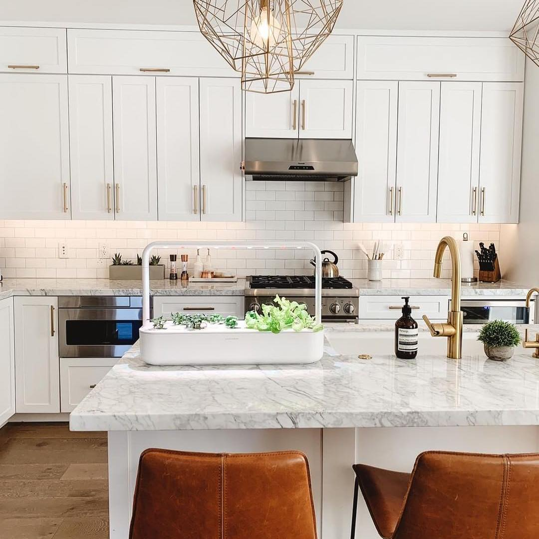 A kitchen with white cabinets and a marble counter top with Click & Grow indoor garden