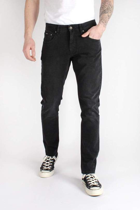 A man wearing a white shirt and black jeans is standing with his hands in his pockets.