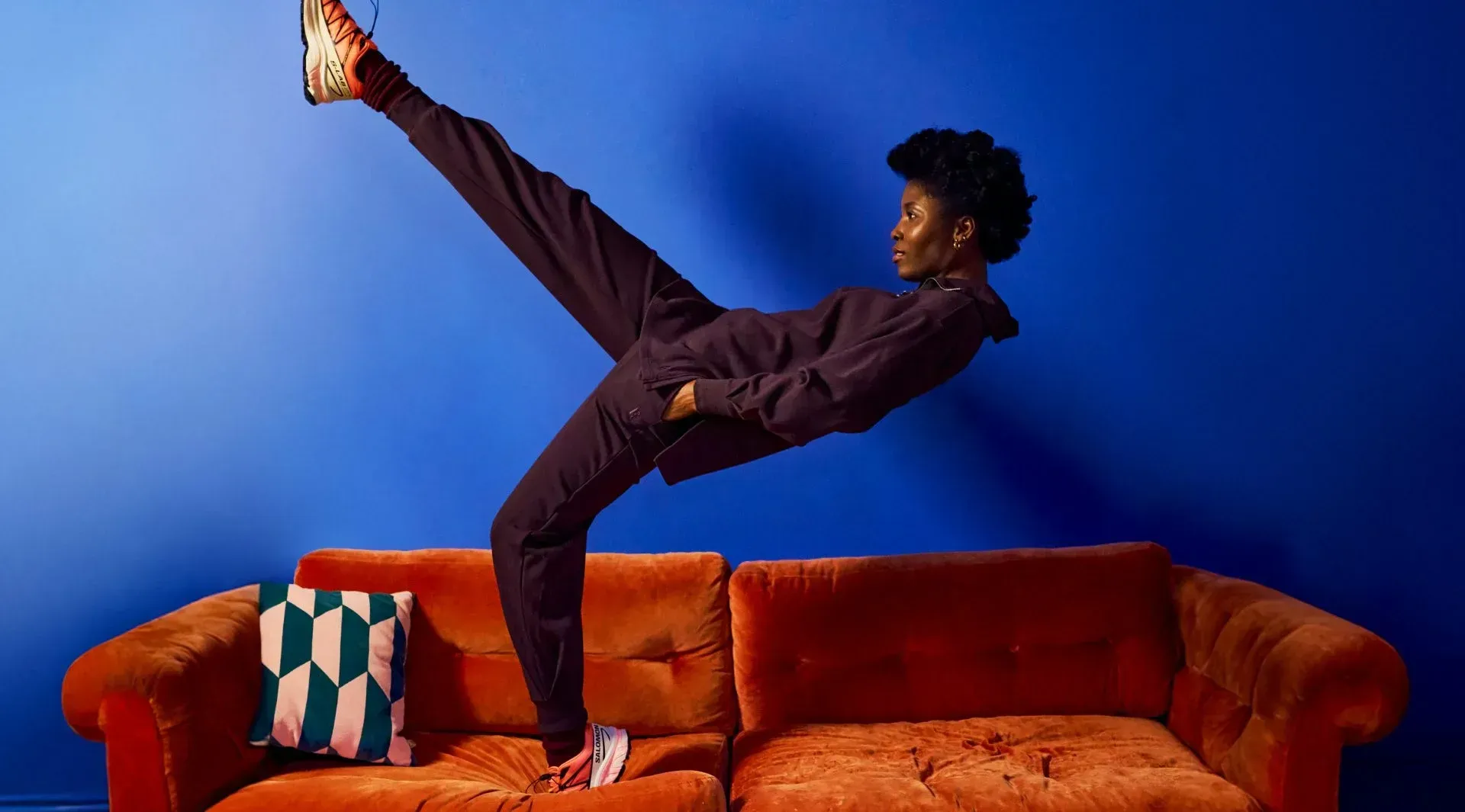 A person is doing a trick on a couch in front of a blue wall.