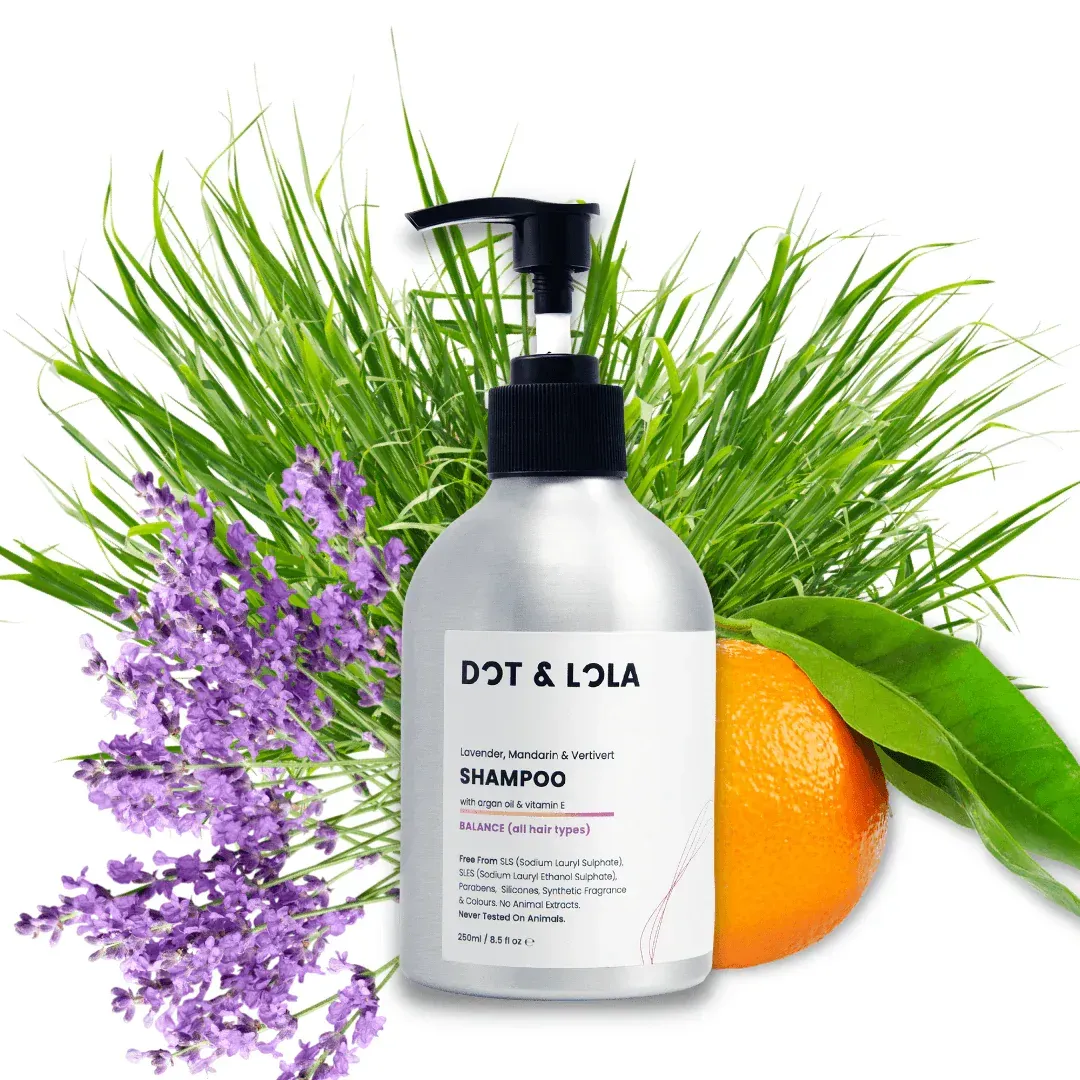 A bottle of dot & lola shampoo is sitting next to a plant and an orange.