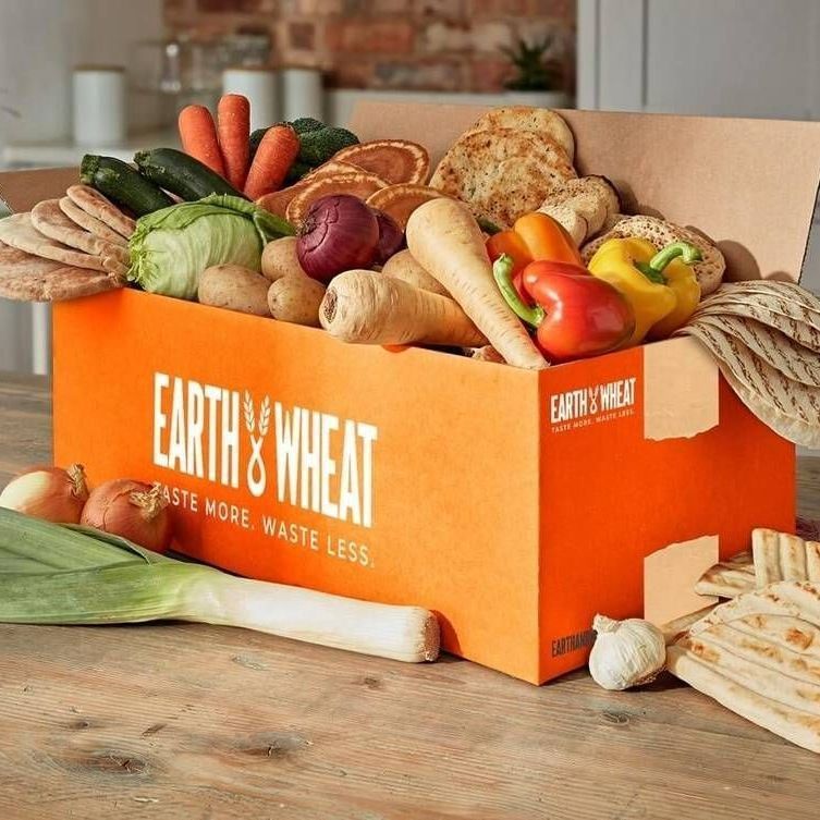 A box filled with vegetables and bread is sitting on a wooden table.