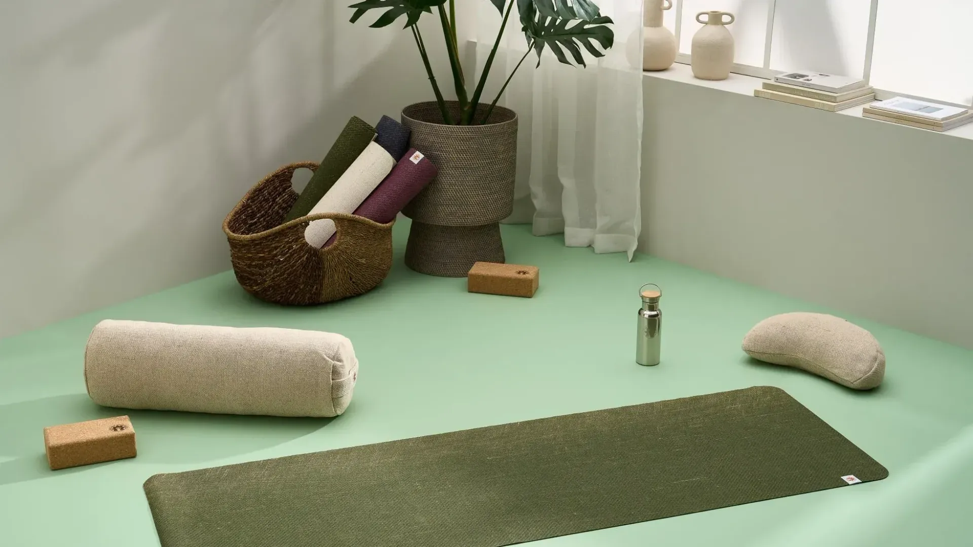 A yoga mat is sitting on a green floor next to a basket of yoga mats.
