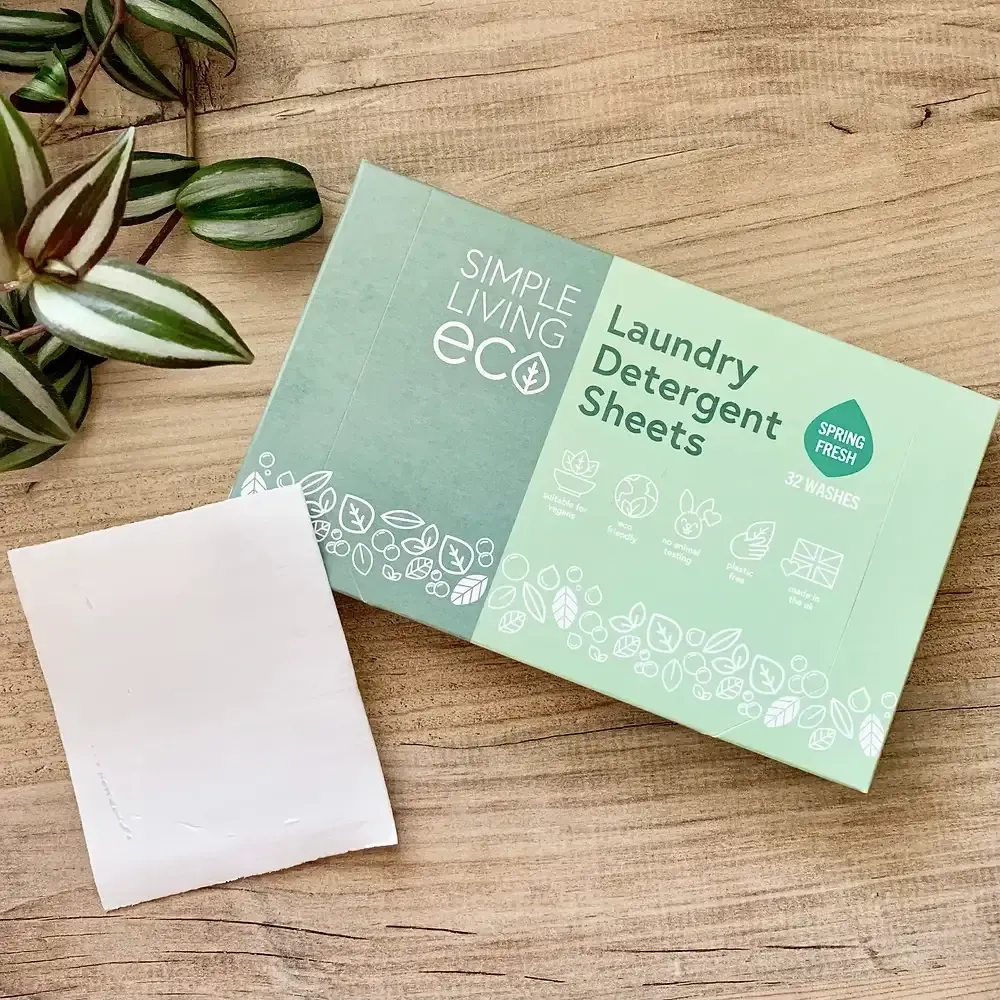 A box of Simple Living Eco laundry detergent sheets is sitting on a wooden table next to a plant.