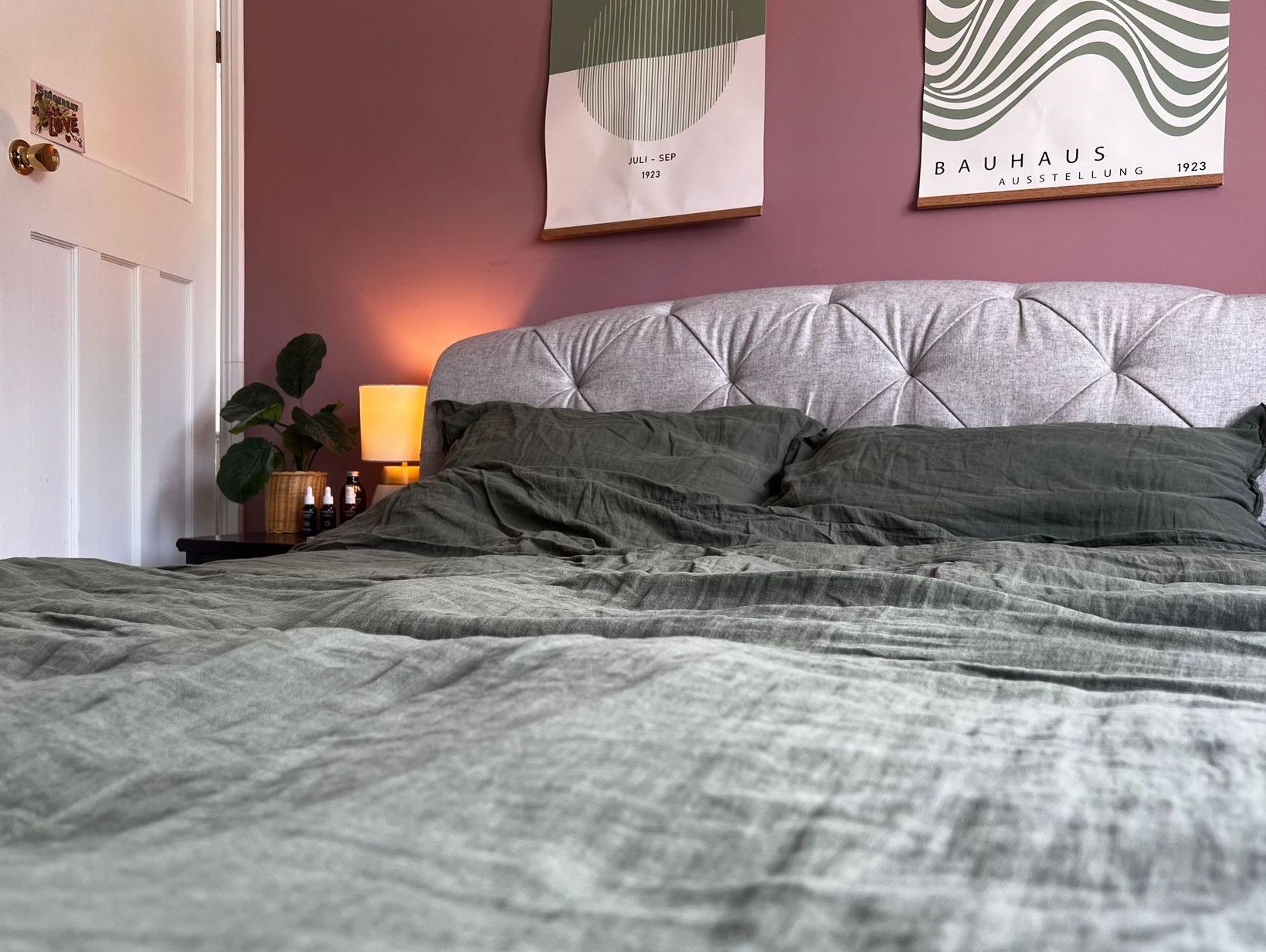 A bed with a headboard and pillows in a bedroom with a pink wall.