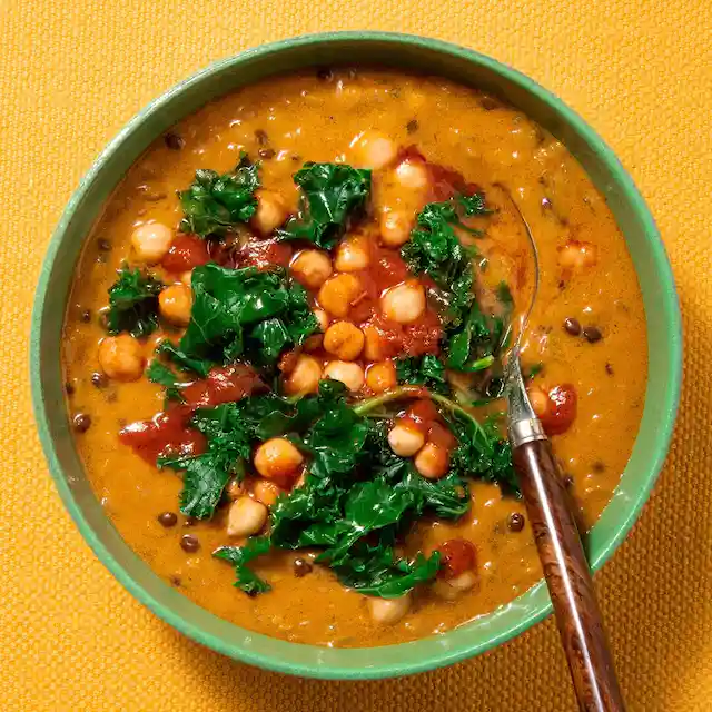 A bowl of soup with chickpeas and kale and a spoon in it