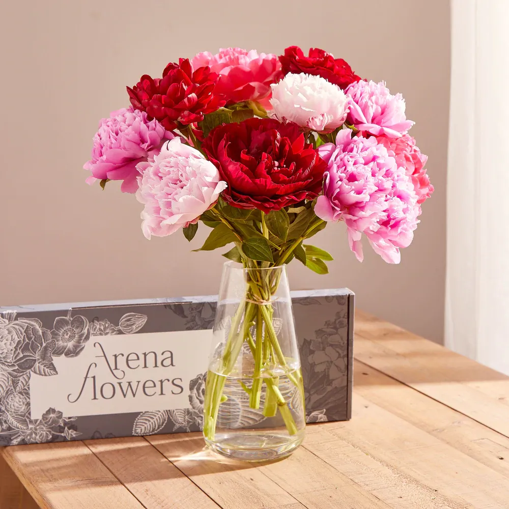 A vase filled with pink and red flowers sits on a wooden table.