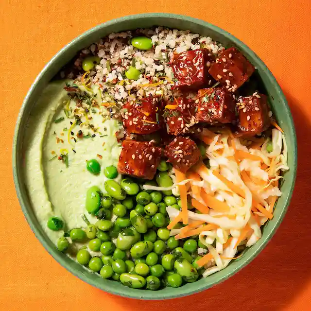A green bowl filled with rice , peas , carrots and meat.
