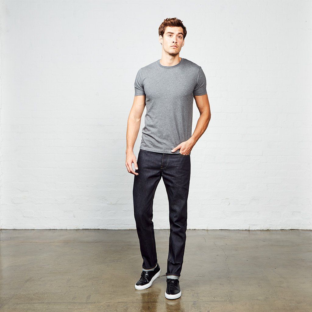 A man wearing a grey t-shirt and jeans is standing in a room.