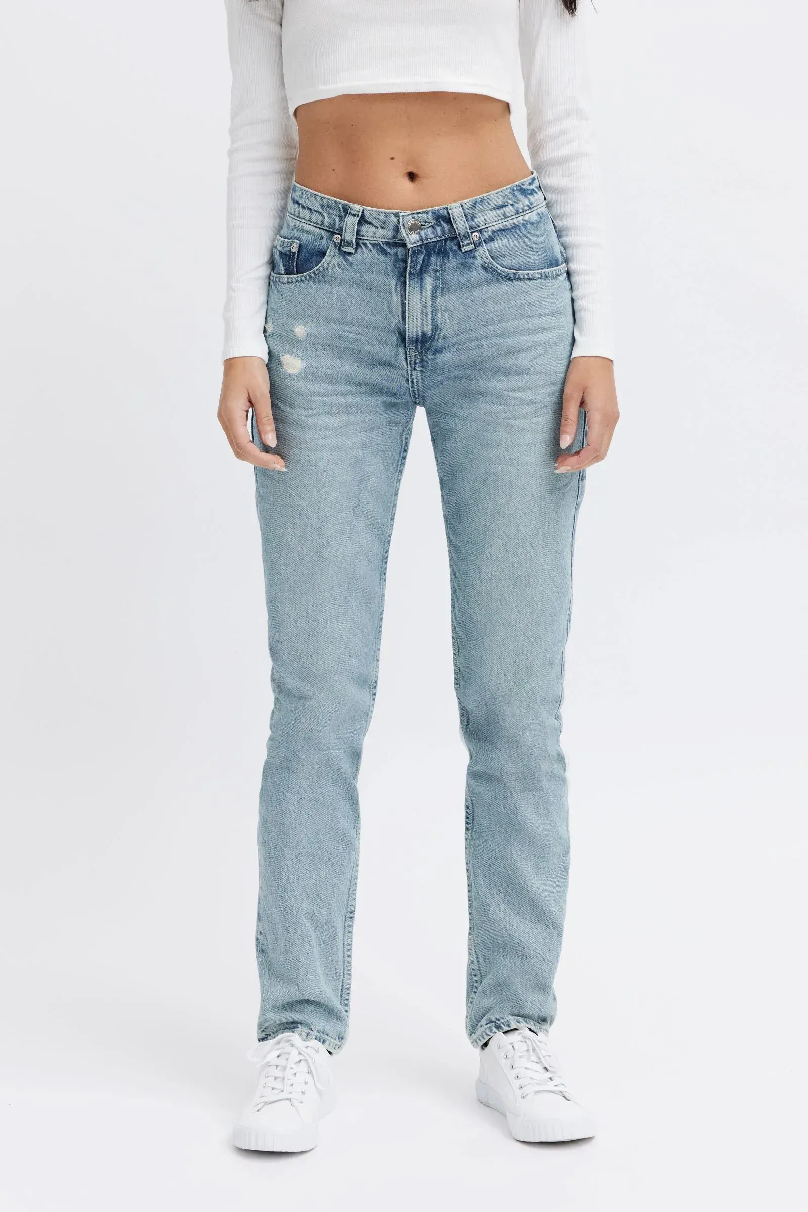 A woman is wearing a white crop top and light blue jeans.