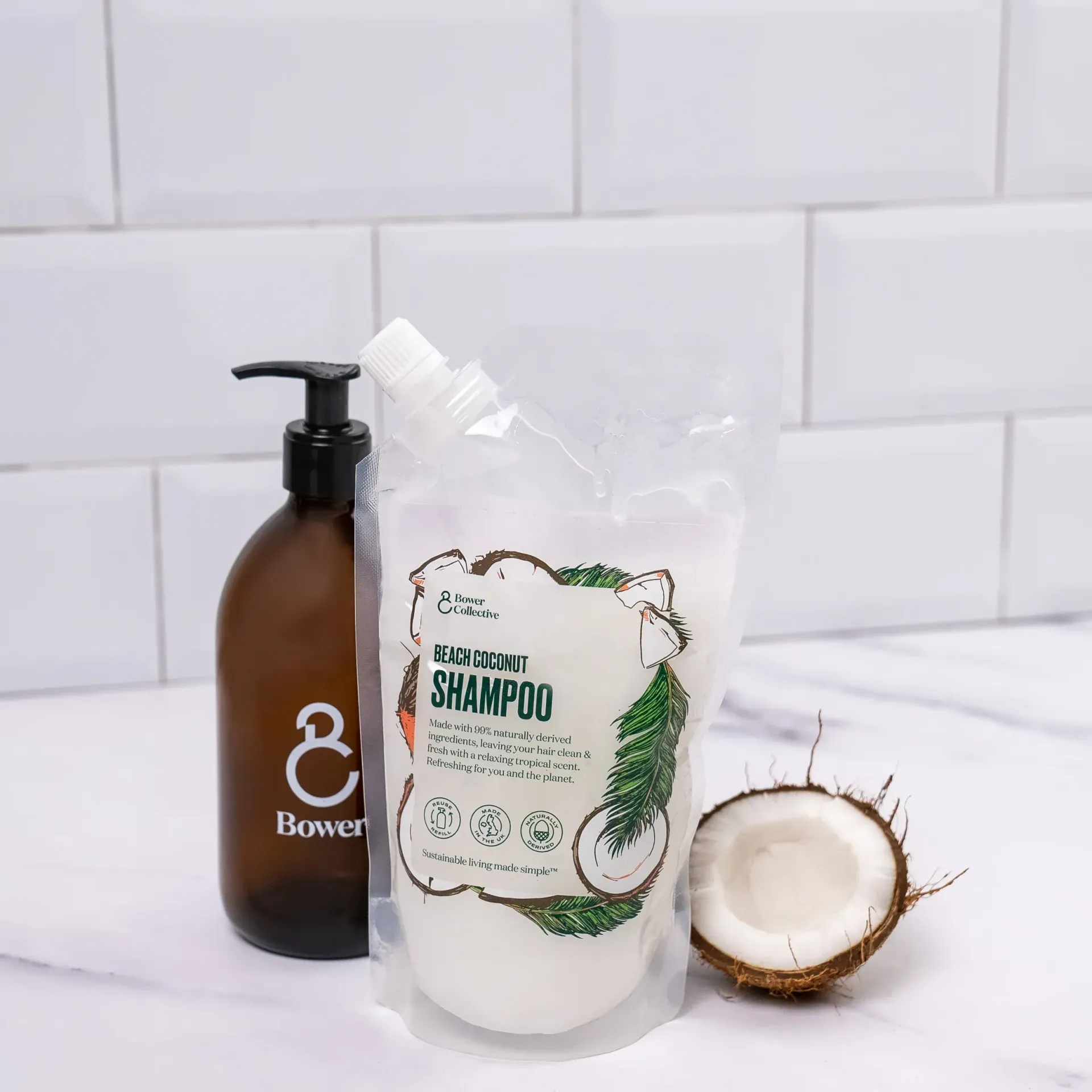 A bottle of Bower Collective shampoo is next to a bag of shampoo and a coconut.