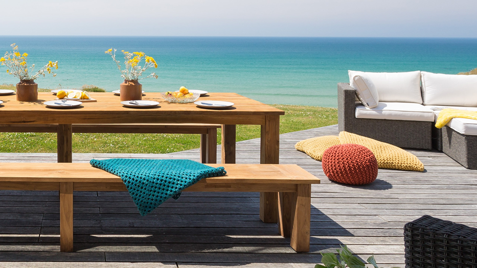 A wooden table and benches on a deck overlooking the ocean.