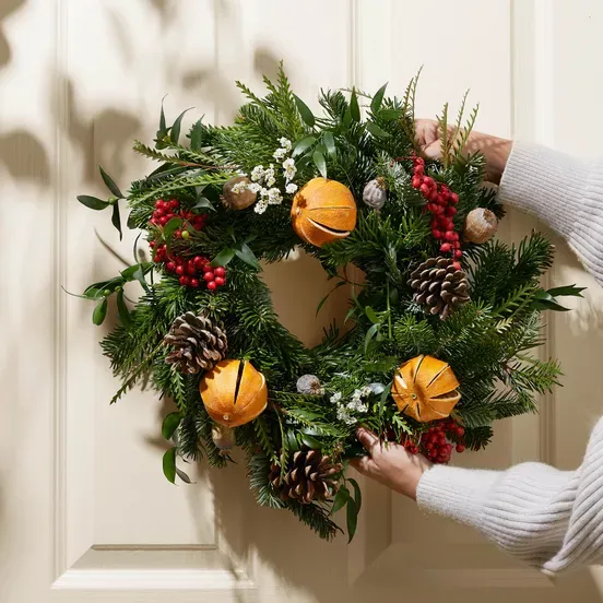 A person is holding a christmas wreath on a door
