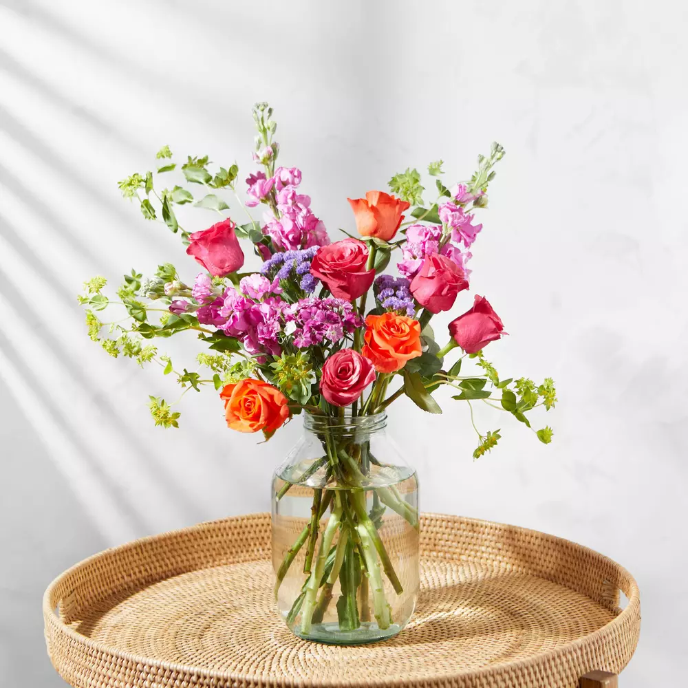 A vase filled with flowers is sitting on a wicker tray on a table.