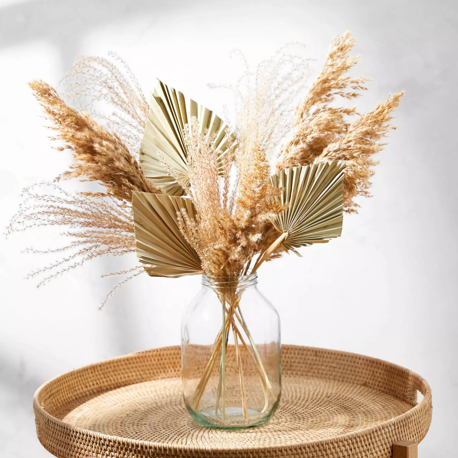 A vase filled with dried flowers is sitting on a wicker tray on a table.
