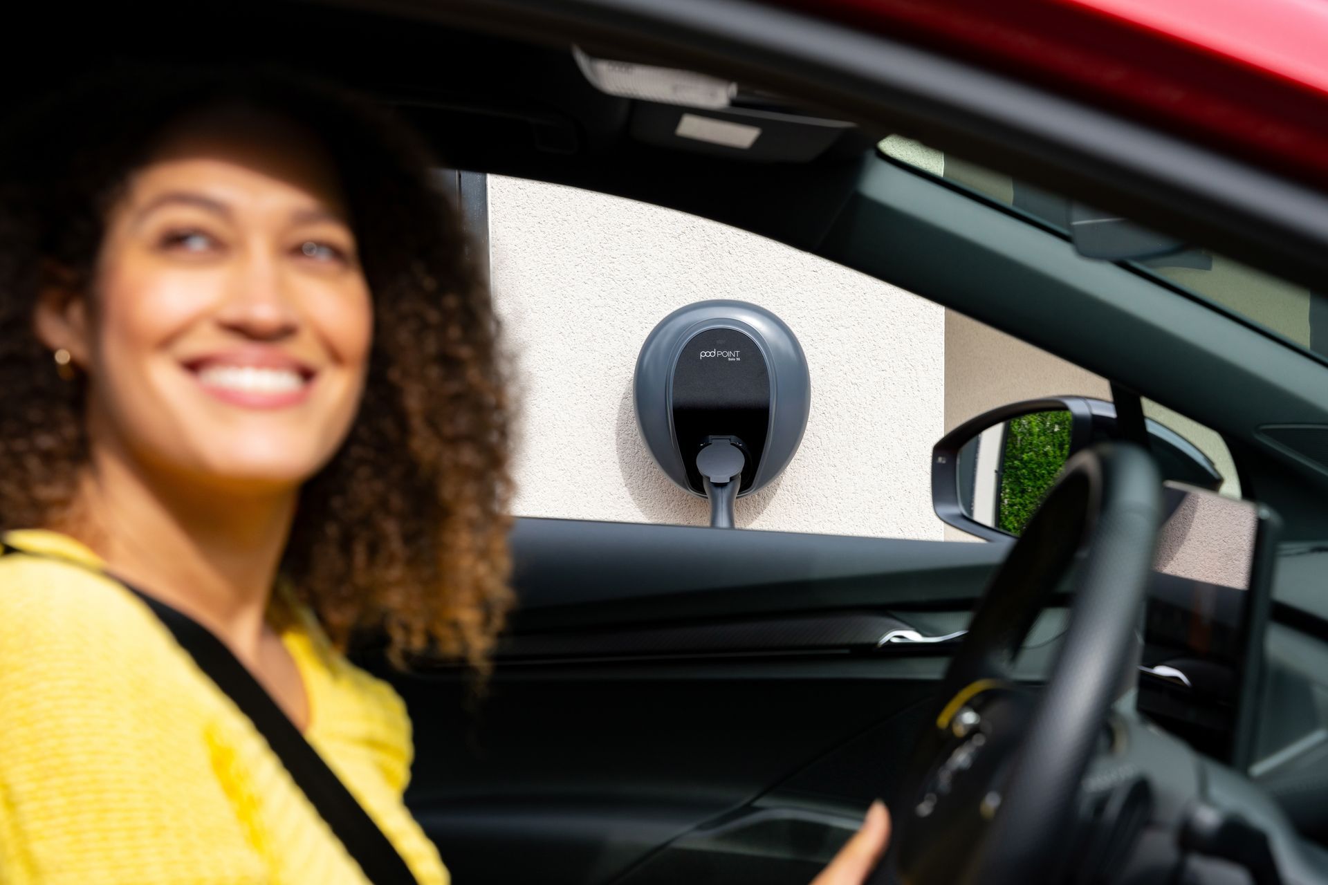 Electric car charging at a station; cable plugged in. Gray vehicle with black tire, charging port open.