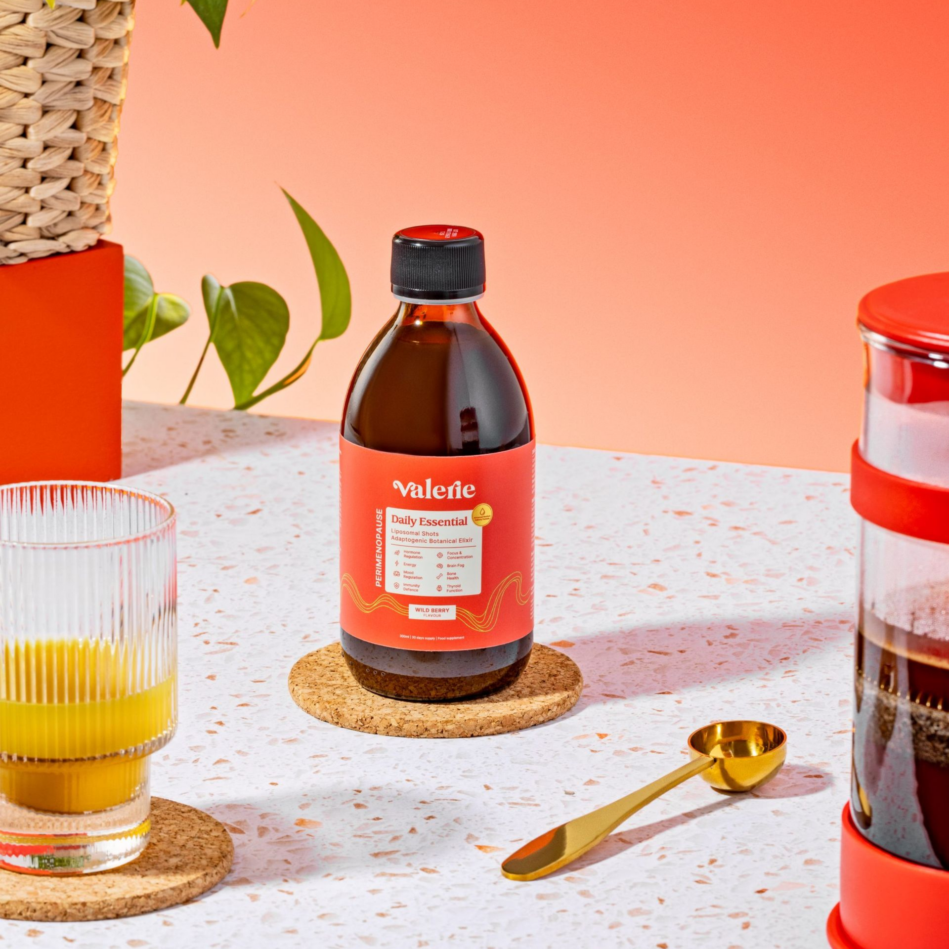 Bottle of syrup on coaster, drink in glass, scoop, and French press on a speckled table.