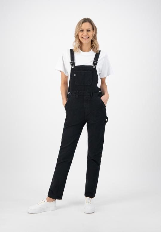 A woman is wearing black overalls and a white t-shirt.