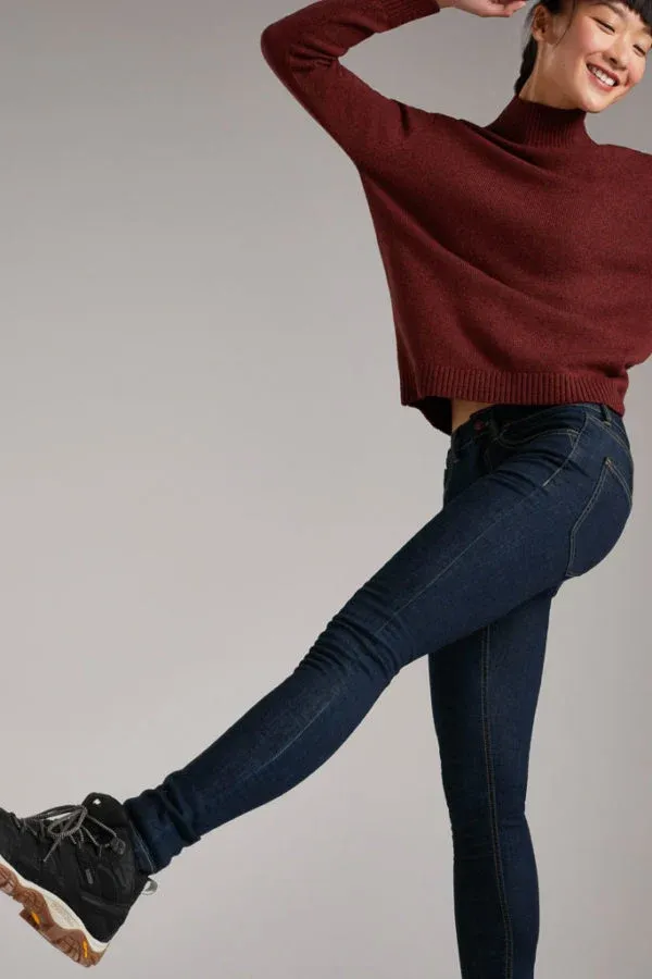 A woman wearing a maroon sweater and blue jeans is standing on one leg