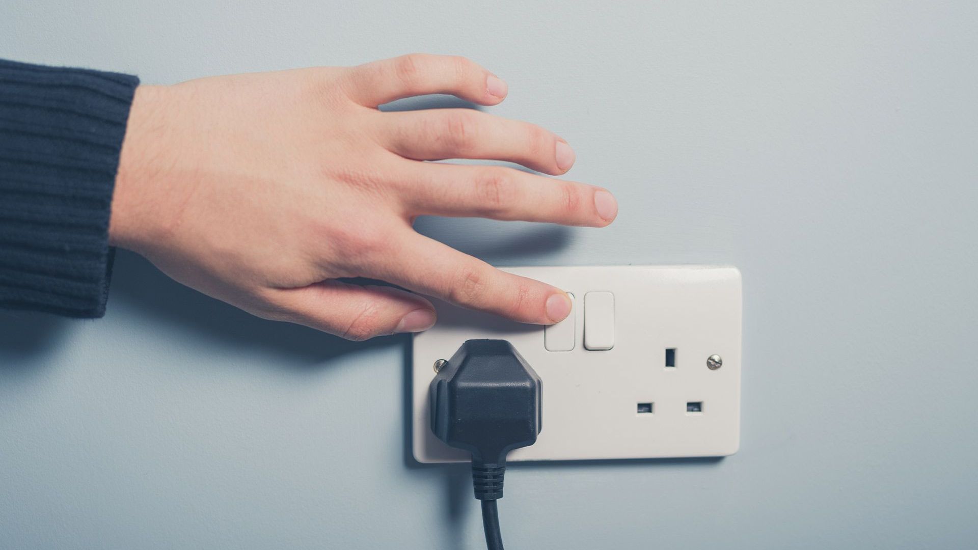 A person is plugging a cord into an electrical outlet.