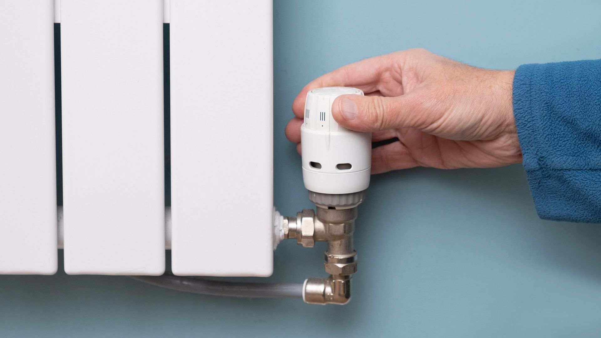 A person is adjusting a thermostat on a radiator.