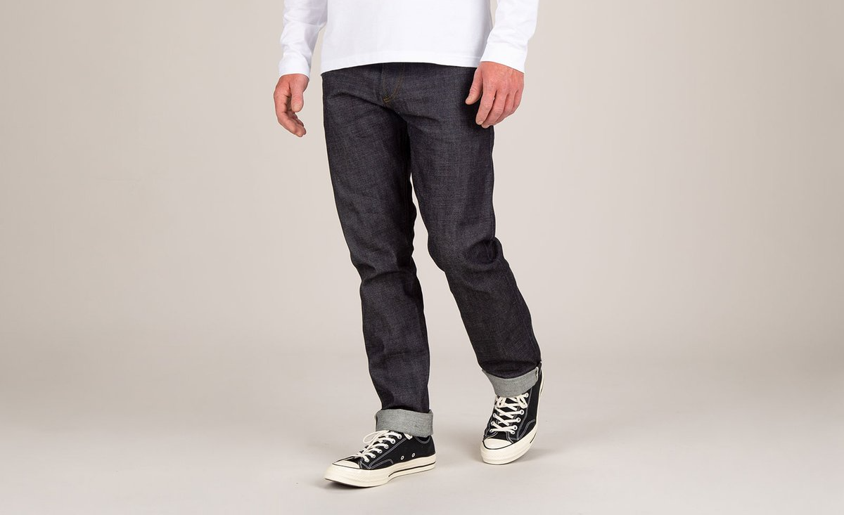 A man wearing a white shirt and black jeans is standing on a white surface.