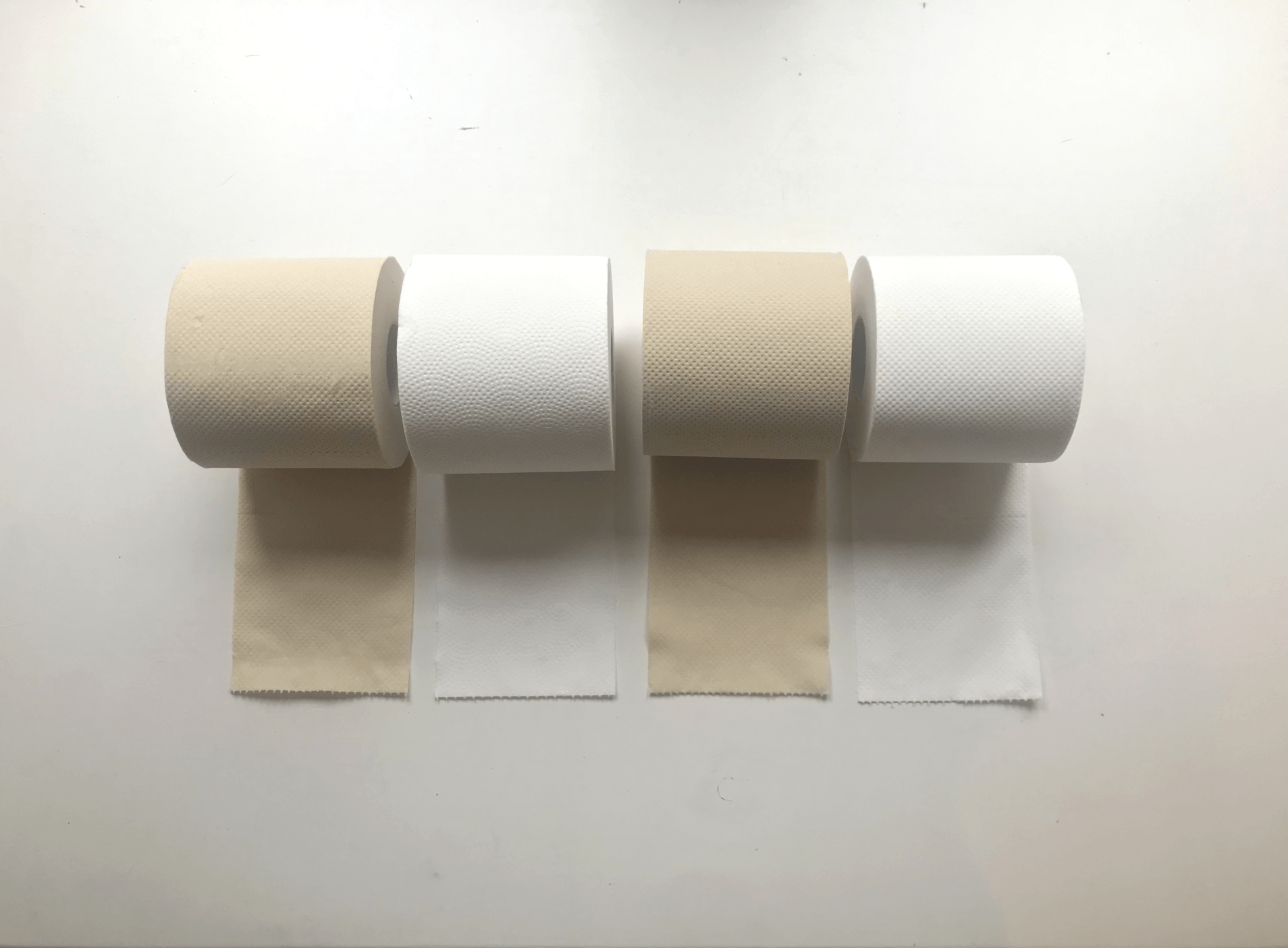 Four rolls of toilet paper are lined up on a white surface.