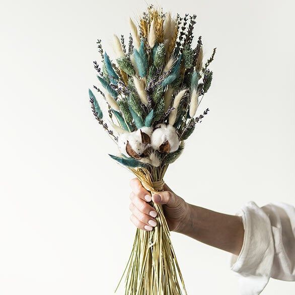 A person is holding a bouquet of dried flowers
