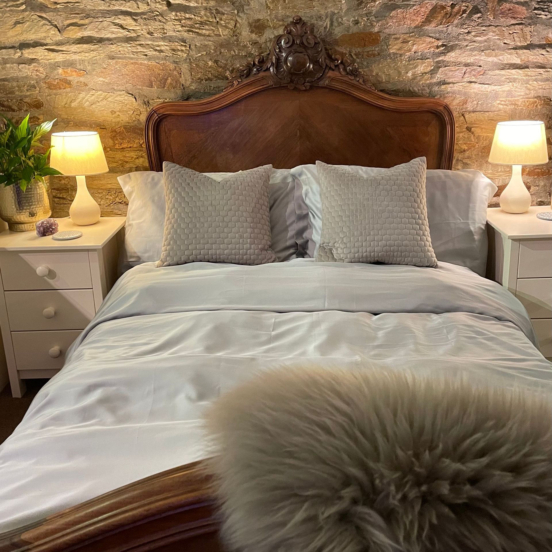a bed with grey eucalyptus silk bed sheets and pillows in front of a stone wall
