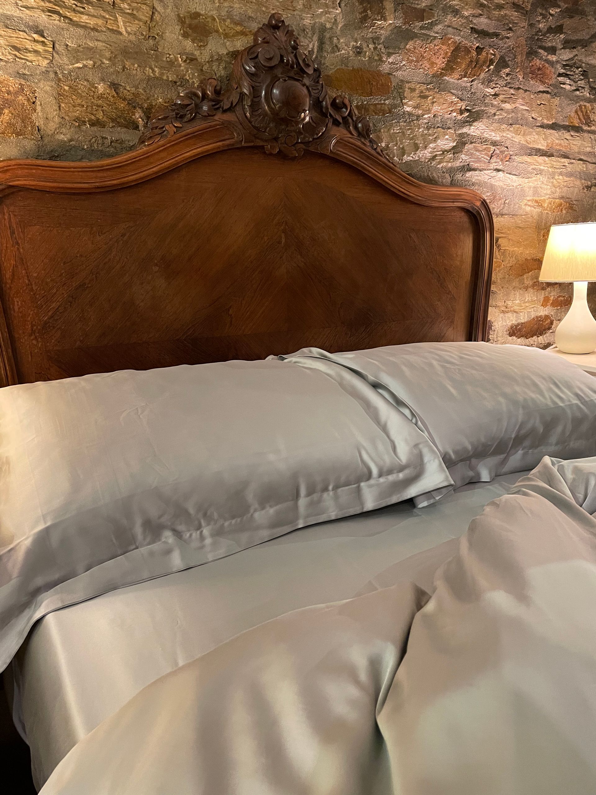 a bed with a french antique wooden headboard and grey silk sheets