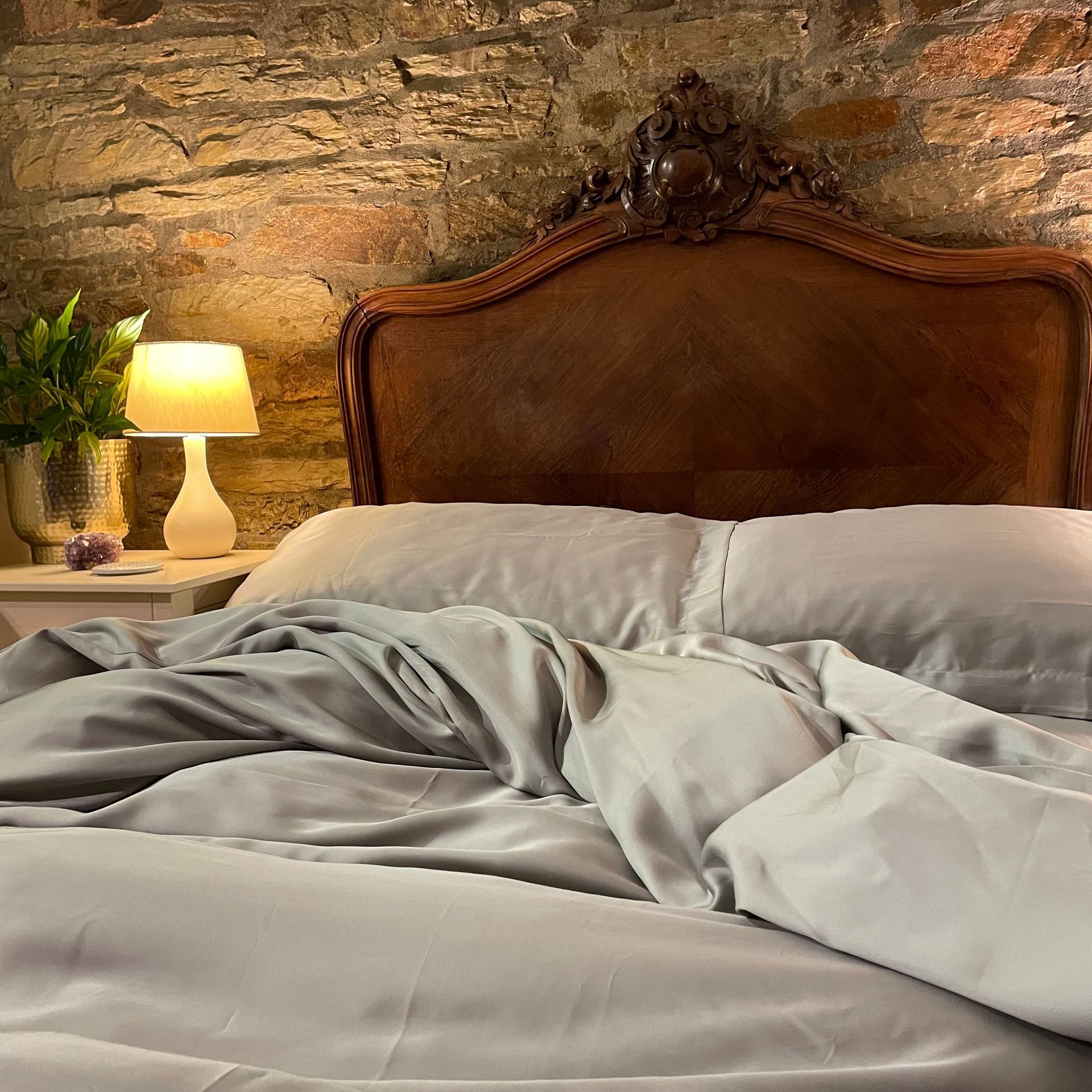a bed with grey ethical bedding sheets and pillows in front of a stone wall