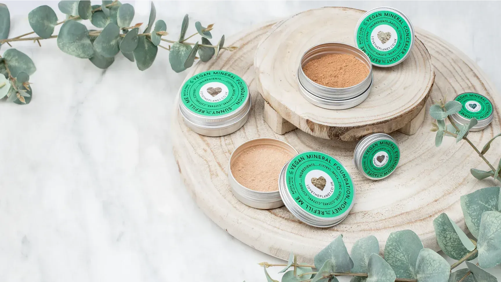 A wooden tray filled with various types of cosmetics and eucalyptus leaves.