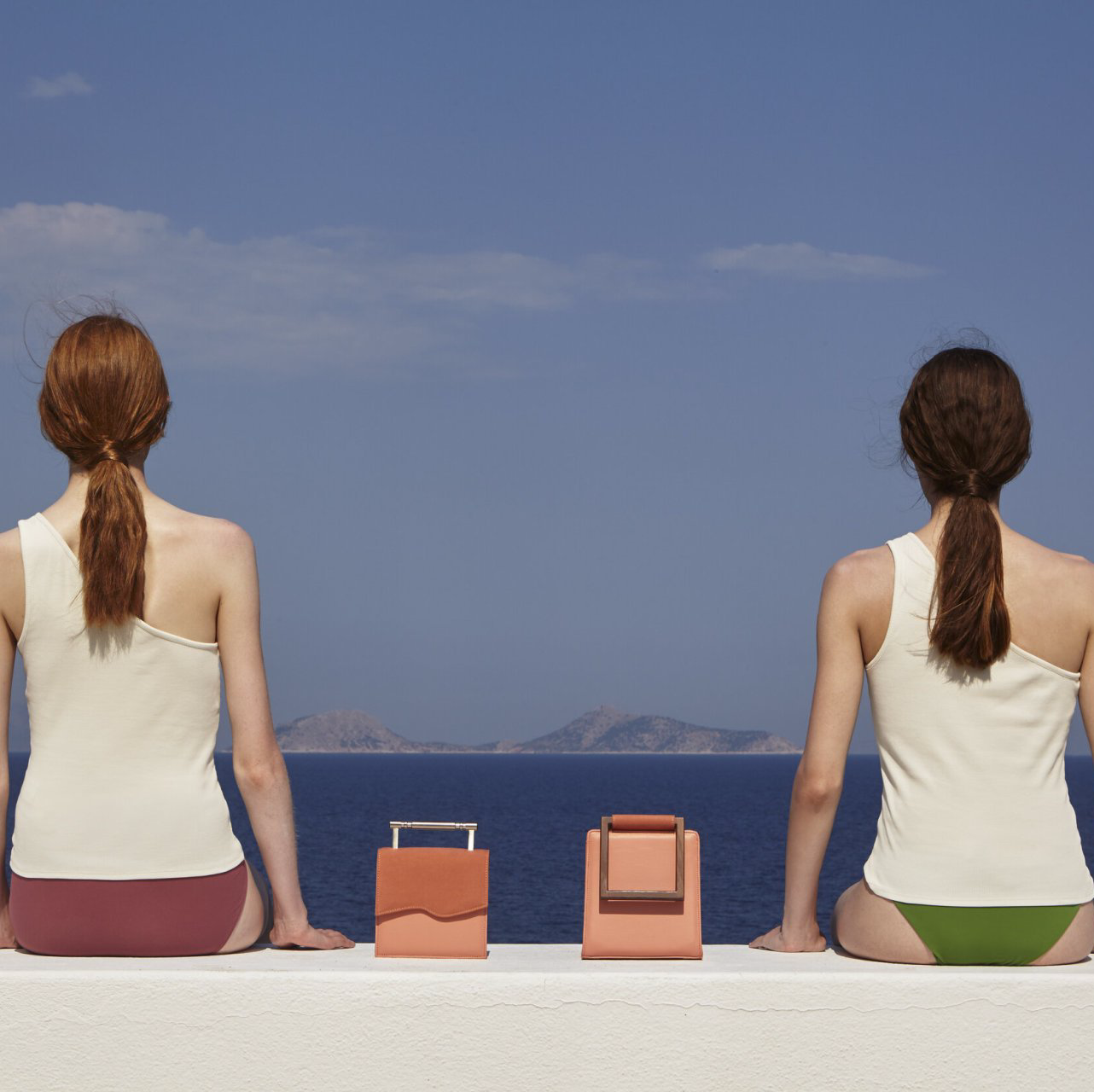 Two women sitting on a wall looking at the ocean