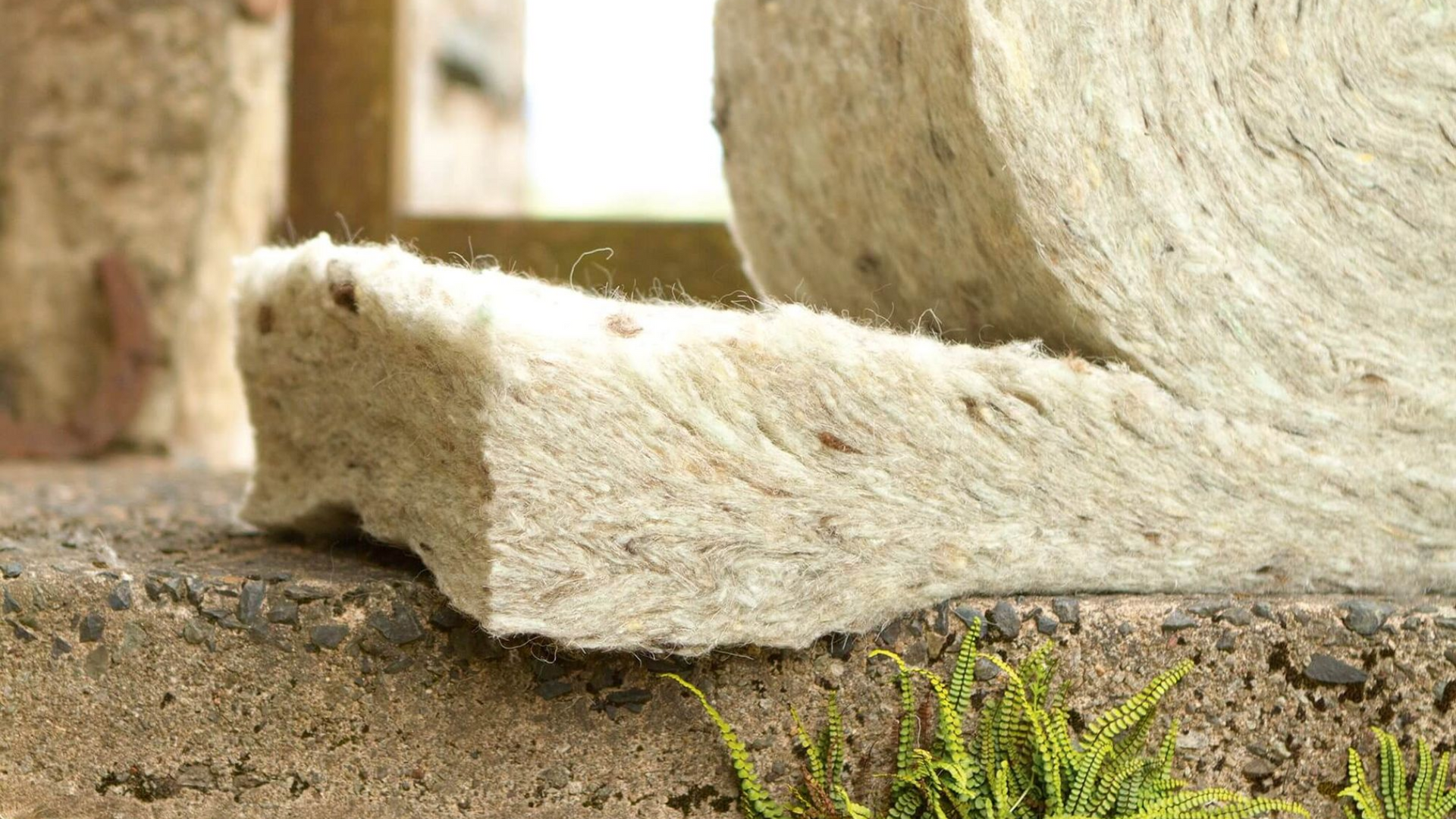Roll of insulation material on a stone surface; beige and brown fibers are visible.