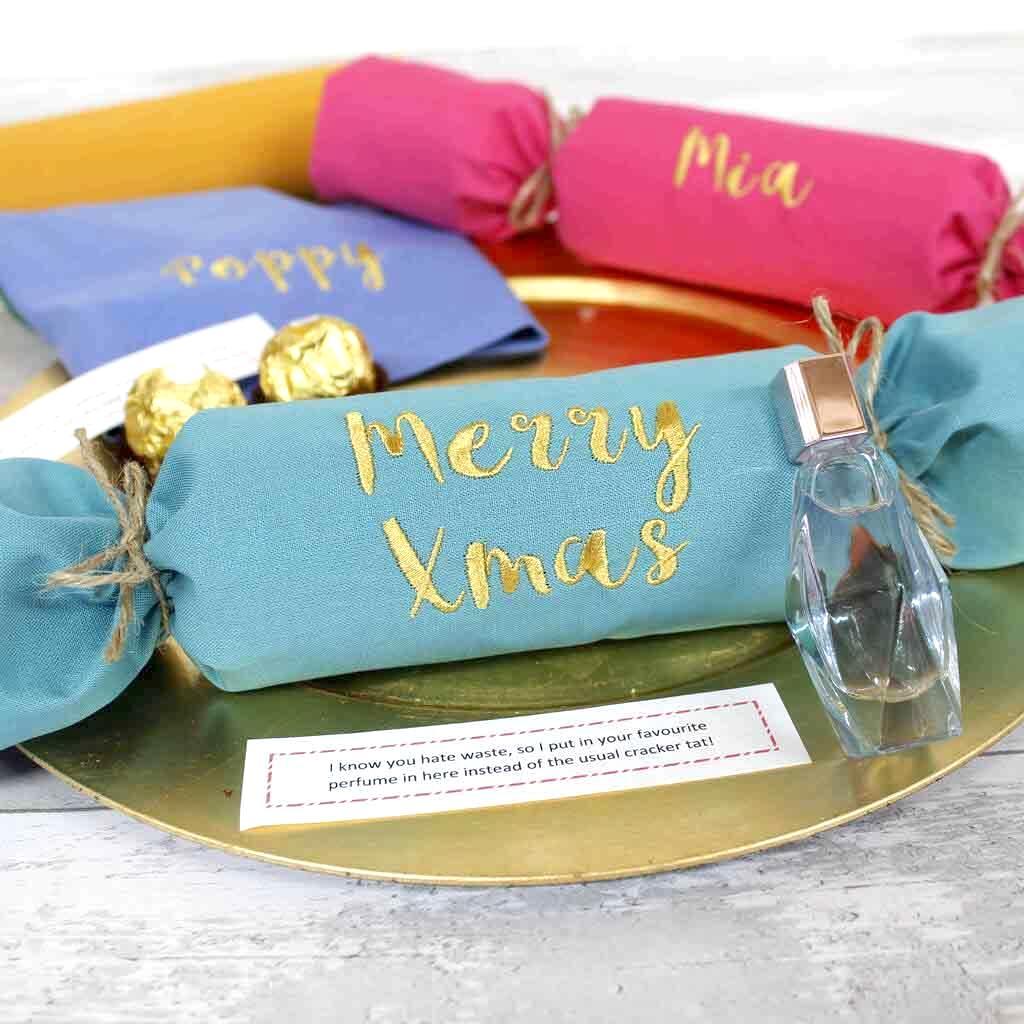 A christmas cracker with the words `` merry xmas '' embroidered on it is sitting on a gold plate.