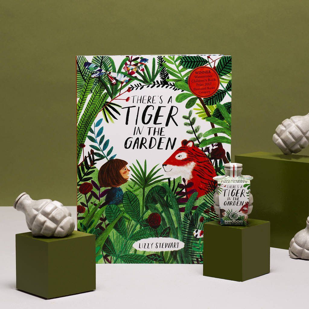 A book called there 's a tiger in the garden is sitting on a table next to a vase.