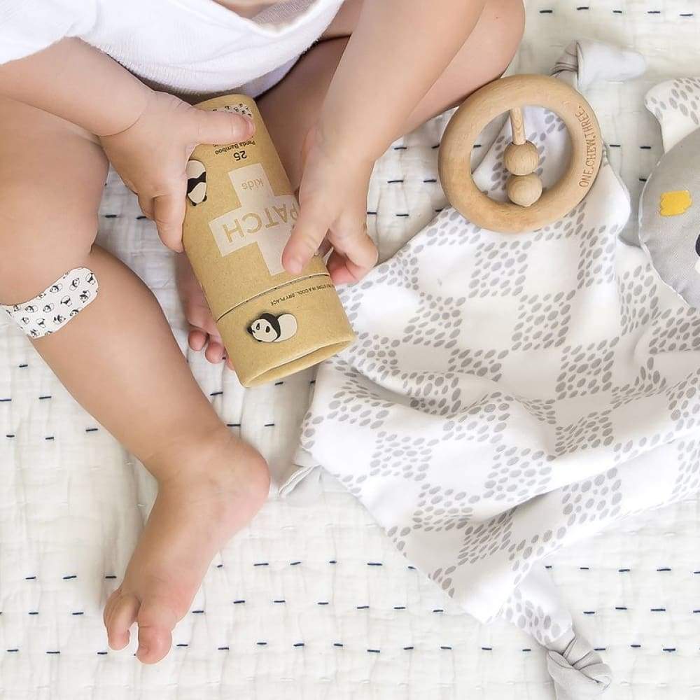 A baby laying on a blanket holding a box of plasters that says patch