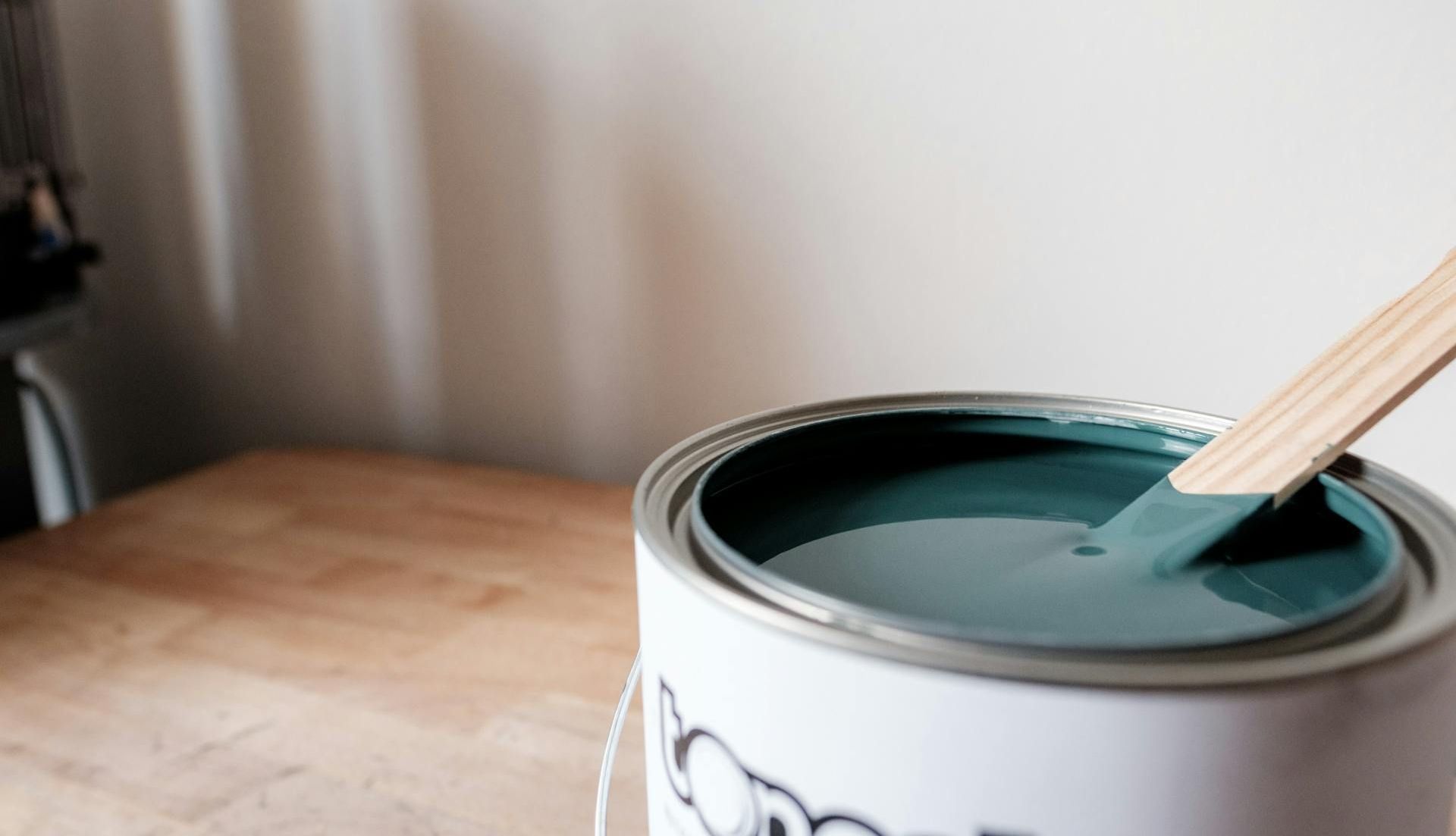 A can of paint with a brush in it is on a wooden table.