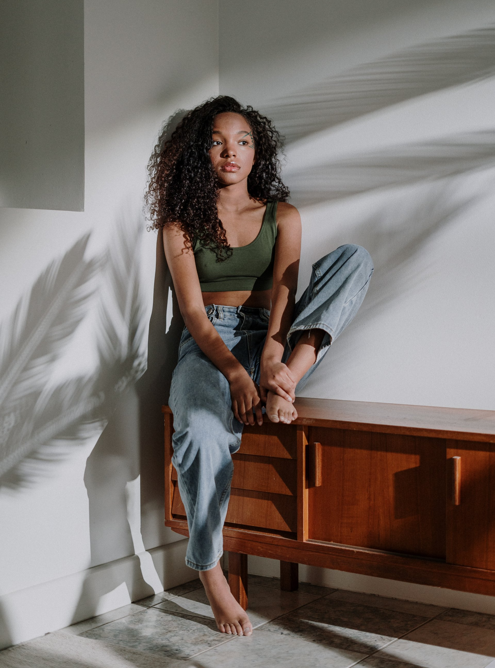 A woman is sitting on a wooden dresser with her legs crossed.