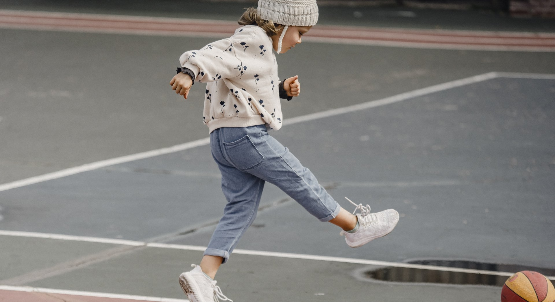 A little girl is kicking a basketball on a basketball court.